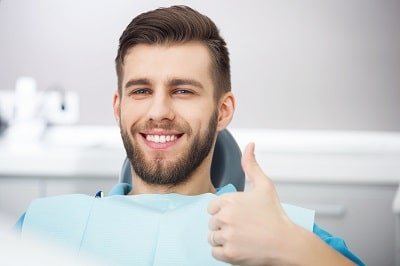 Portrait of happy patient in dental chair giving a thumbs up